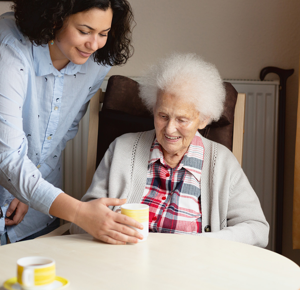 Caregiver handing an elderly woman a cup of tea